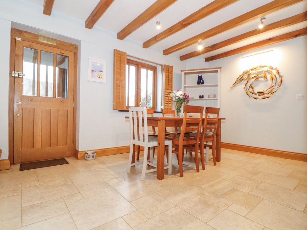 A dining room with a wooden table and chairs near a window with wooden shutters at Splatt Barn in Rock