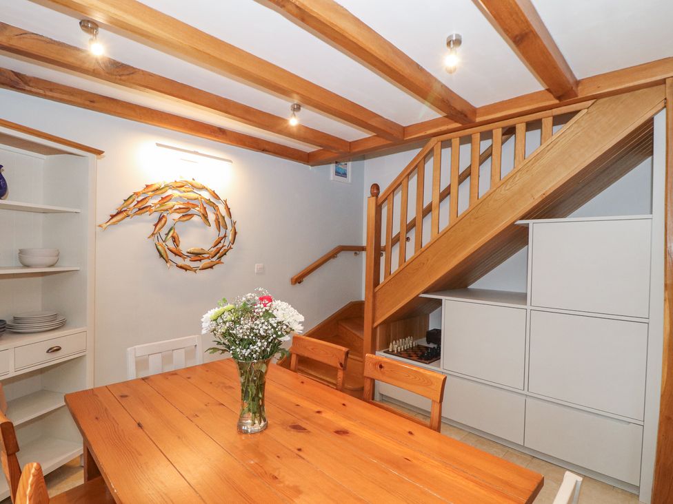 A dining area with wooden table and chairs a flower vase on the table wooden ceiling beams white shelving unit and wall art of fish at Splatt Barn Rock