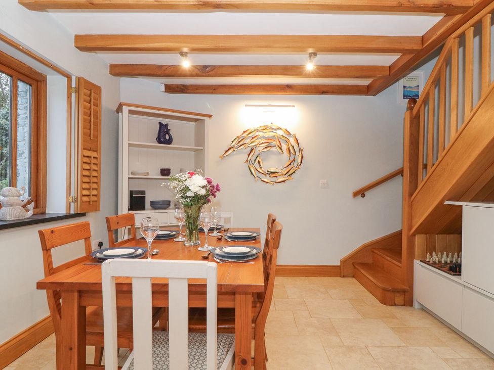 A dining room with a wooden table set for six, wooden chairs, a flower vase, a bookshelf, wooden stairs, and fish wall decor at Splatt Barn in Rock