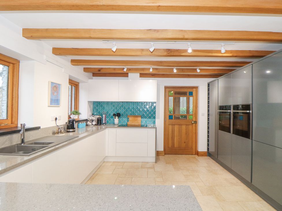A kitchen with white cabinets wooden ceiling beams and a wooden door at Splatt Barn in Rock