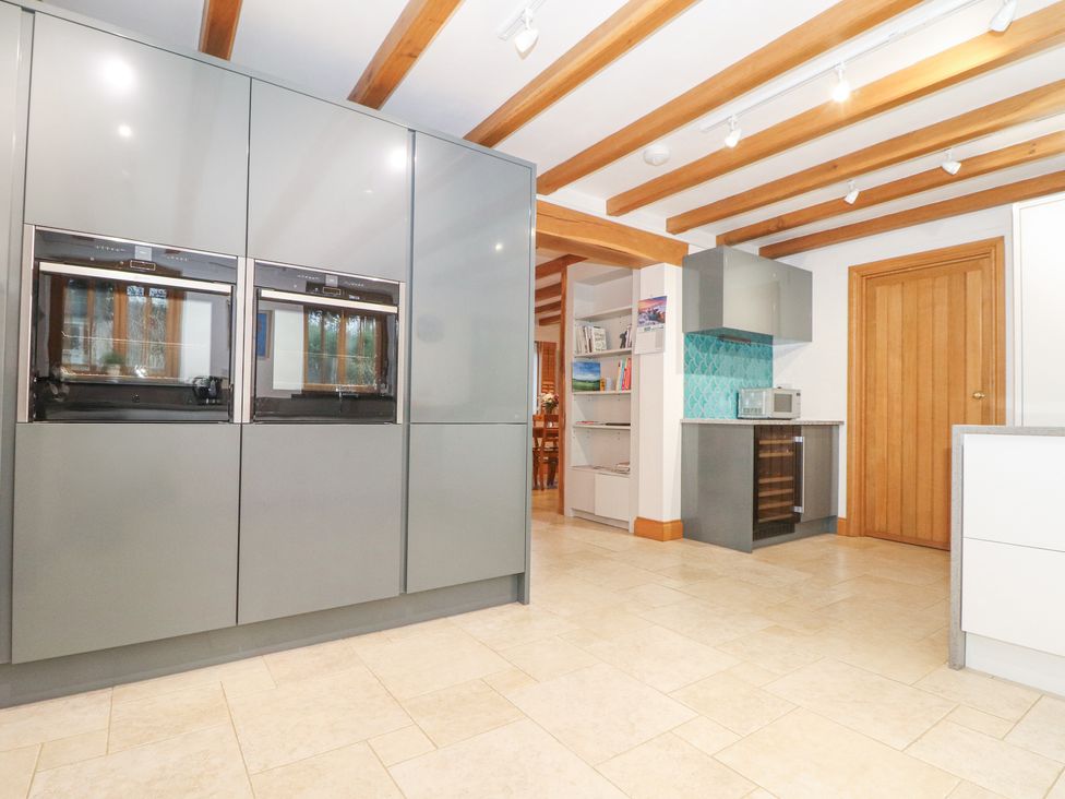 A kitchen with built in ovens grey cabinets a wine cooler a microwave wooden door and exposed wooden ceiling beams at Splatt Barn in Rock