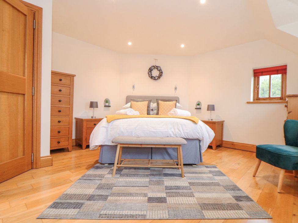 A bedroom with a bed with pillows and towels a bench a patterned rug wooden furniture and a green chair at Splatt Barn in Rock