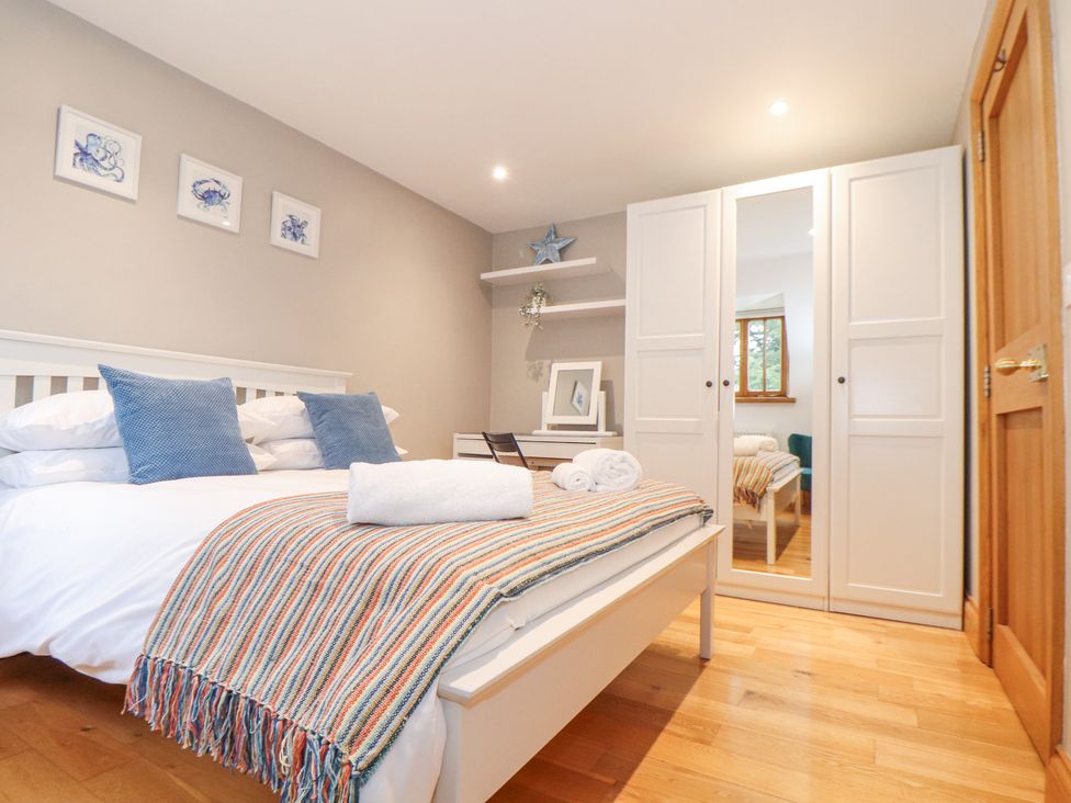 A bedroom with a bed with blue pillows and striped blanket a wardrobe with mirrored door and wooden flooring at Splatt Barn in Rock