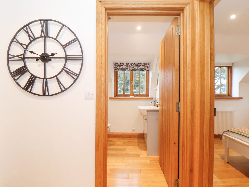 A hallway with a large wall clock and a wooden door leading to a bathroom and bedroom at Splatt Barn in Rock