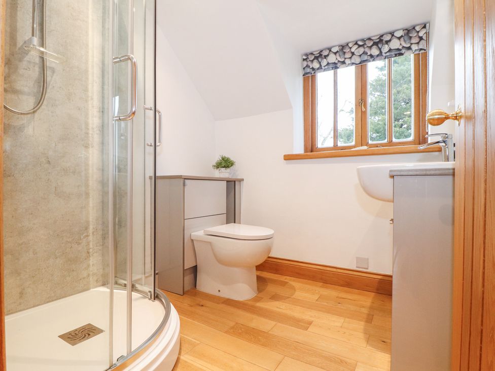 A bathroom with a shower enclosure a toilet a sink and a window with a stone patterned blind at Splatt Barn in Rock