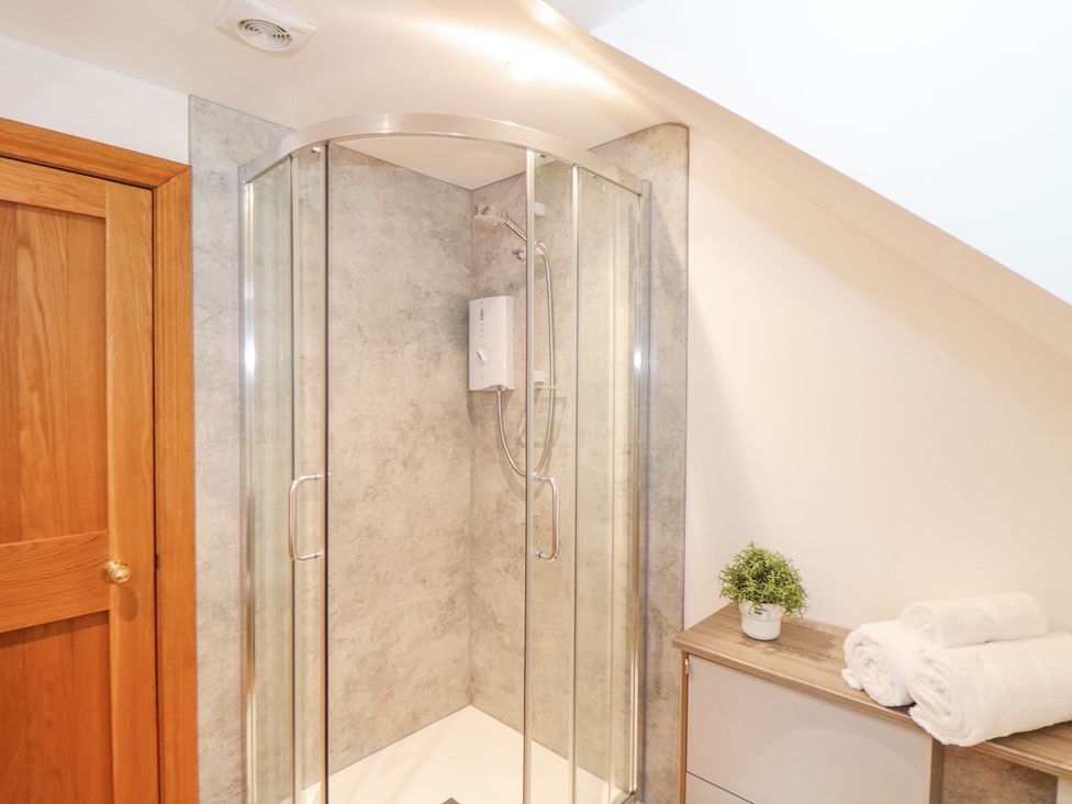 A bathroom with a corner glass shower enclosure a wooden door a cabinet with rolled towels and a small potted plant at Splatt Barn in Rock