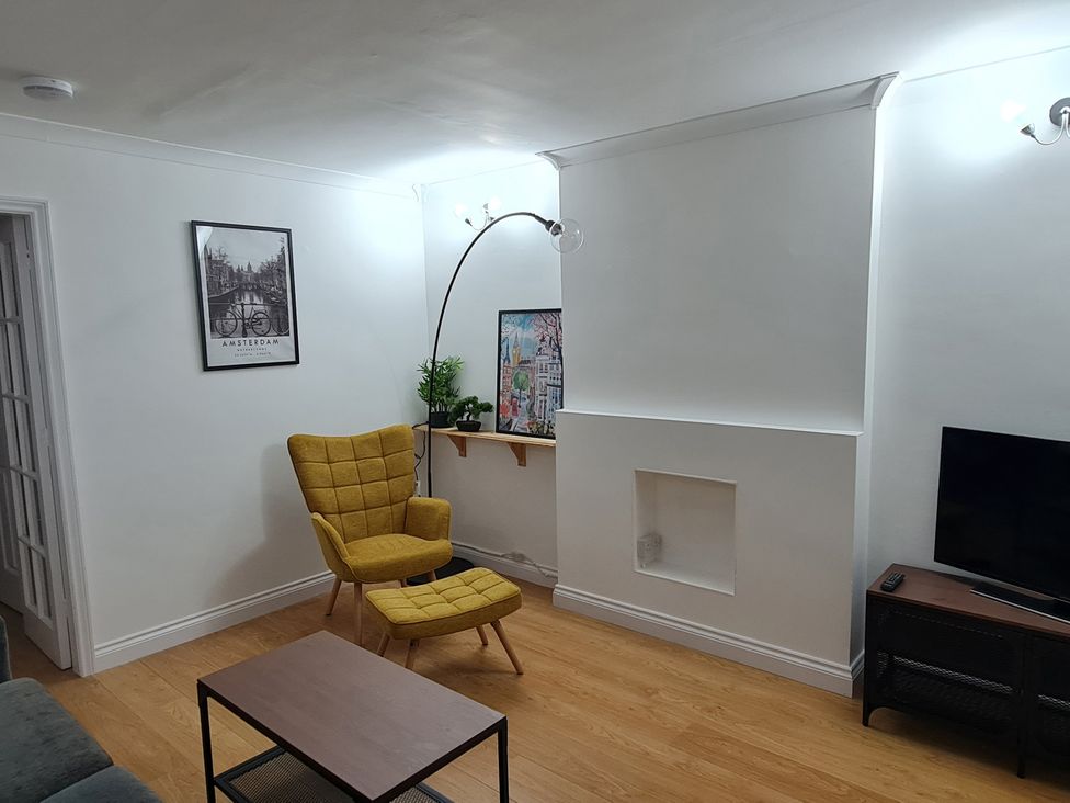 A living room with a yellow chair, table, and wall art at 12 Gorse Lane in Leicester
