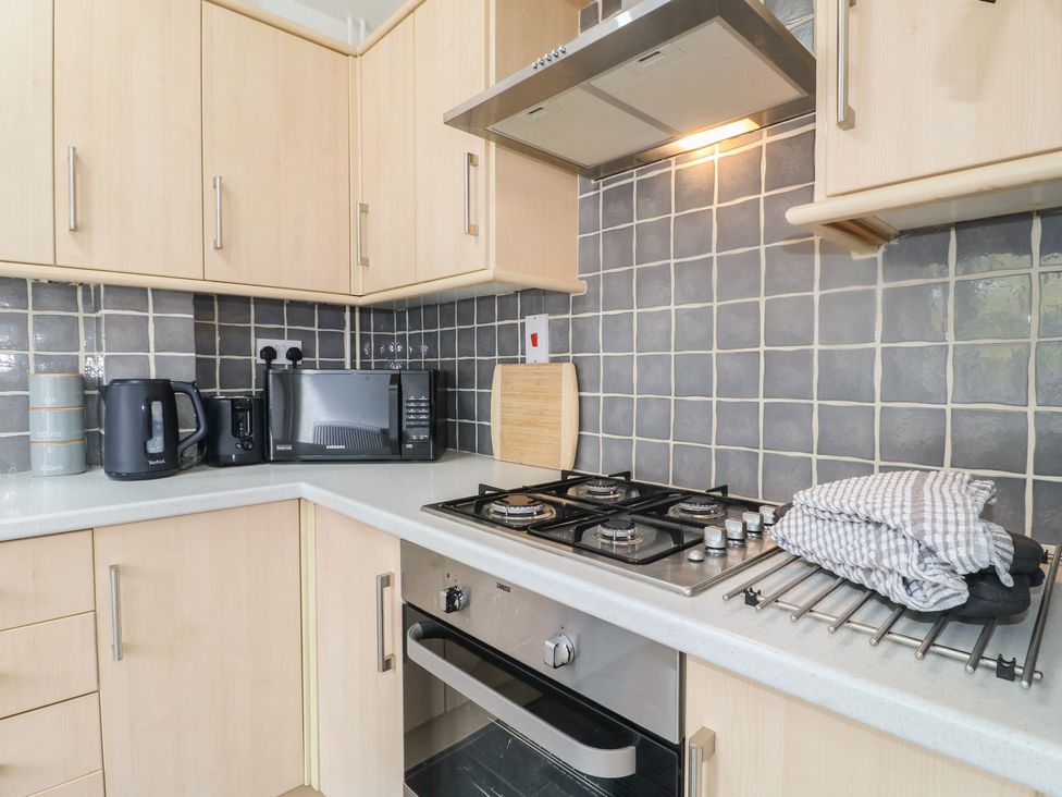 A kitchen with cabinets, hob, microwave, kettle, and cutting board at 12 Gorse Lane in Syston