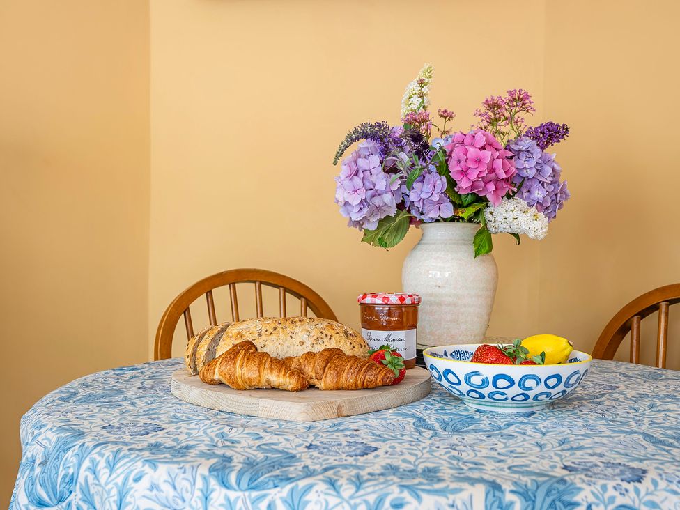 A dining table with croissants, jam, fruit bowl and flowers at Bodior Lodge in Rhoscolyn