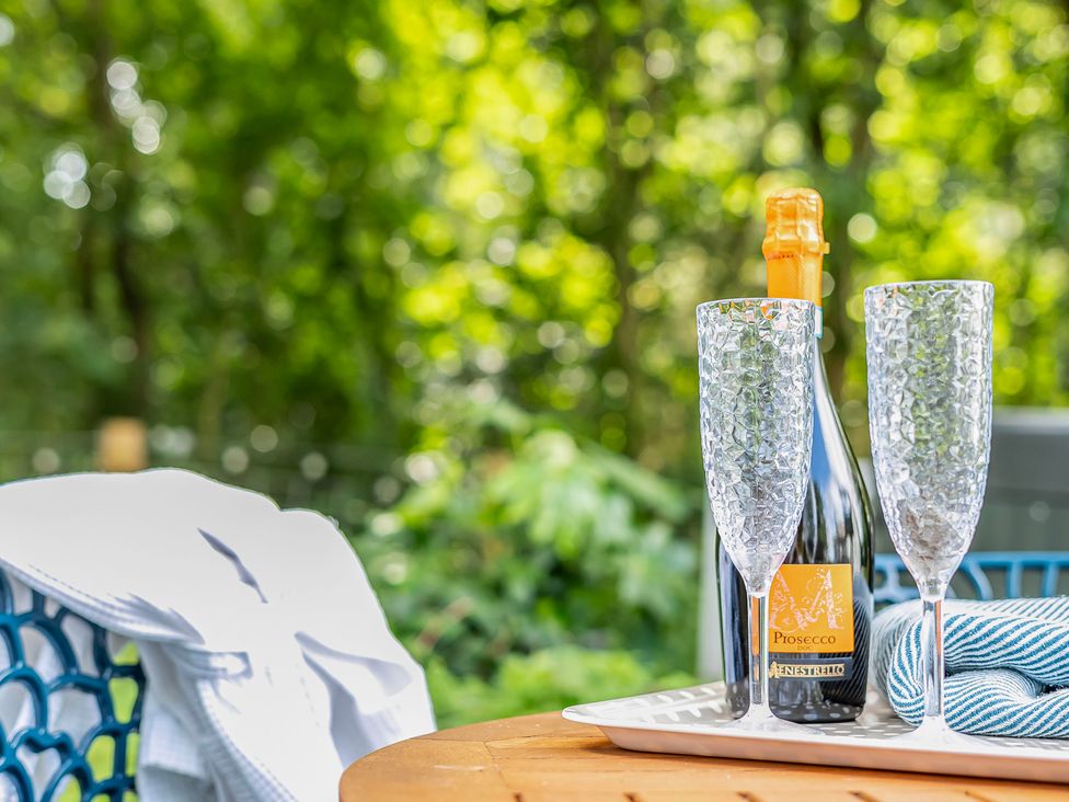 Bottle of Prosecco and glasses on a tray in an outdoor seating area at Bodior Lodge Rhoscolyn