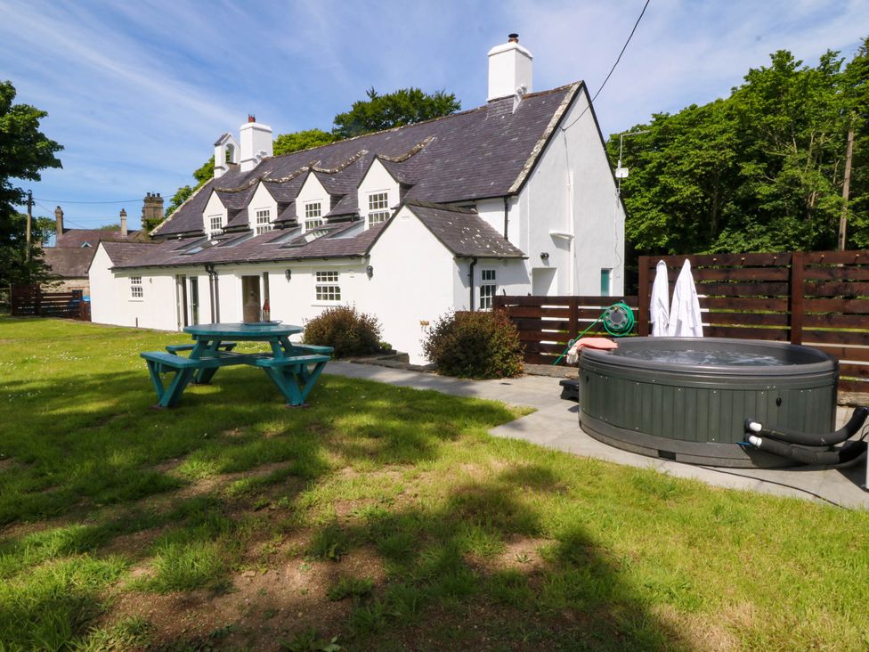 An outdoor area with a white cottage building a blue picnic table and a round hot tub in the grass at Bodior Garden Cottage in Rhoscolyn