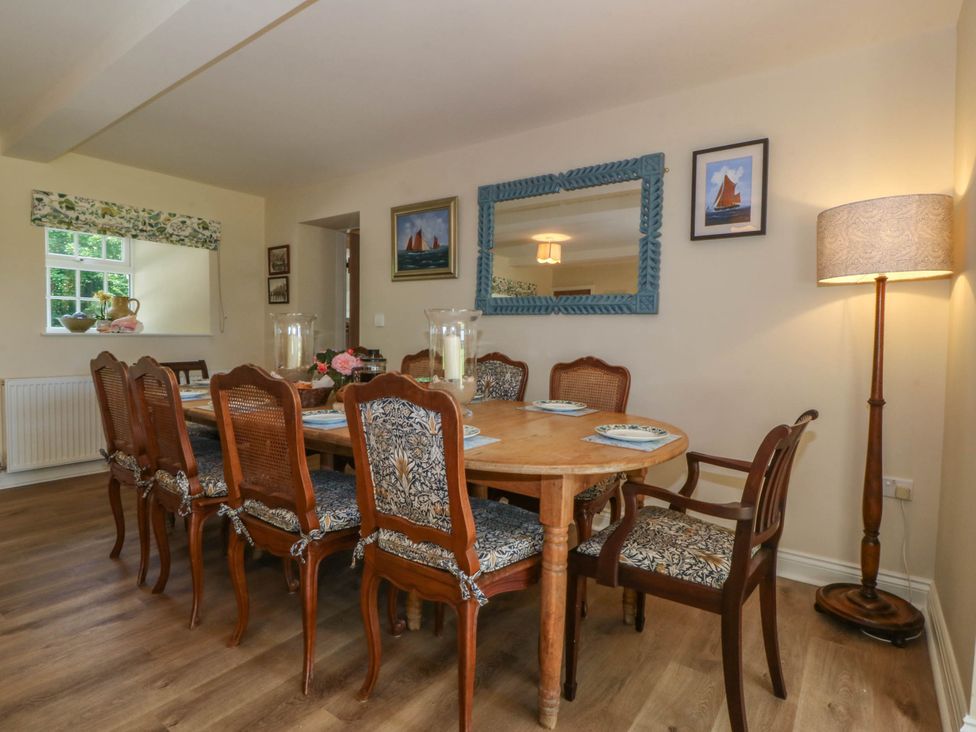A dining room with a wooden table and eight chairs a floor lamp two paintings and a large mirror on the wall at Bodior Garden Cottage in Rhoscolyn