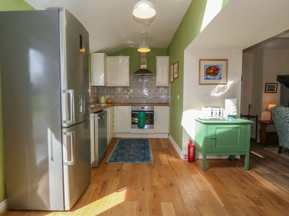 A kitchen with stainless steel refrigerator oven and dishwasher green walls and wooden floor at Bodior Garden Cottage in Rhoscolyn