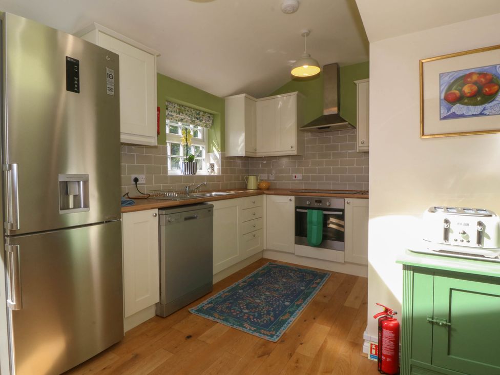A kitchen with a stainless steel fridge dishwasher oven and a green cabinet with a toaster at Bodior Garden Cottage in Rhoscolyn