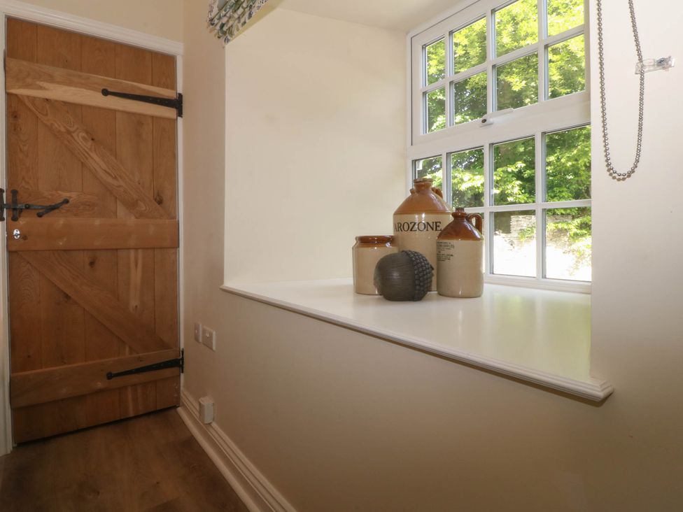 A wooden door next to a window with four ceramic jugs and a decorative object on the windowsill at Bodior Garden Cottage in Rhoscolyn