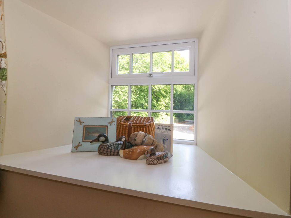 A window sill with a framed picture basket decorative duck figurines and a book at Bodior Garden Cottage in Rhoscolyn