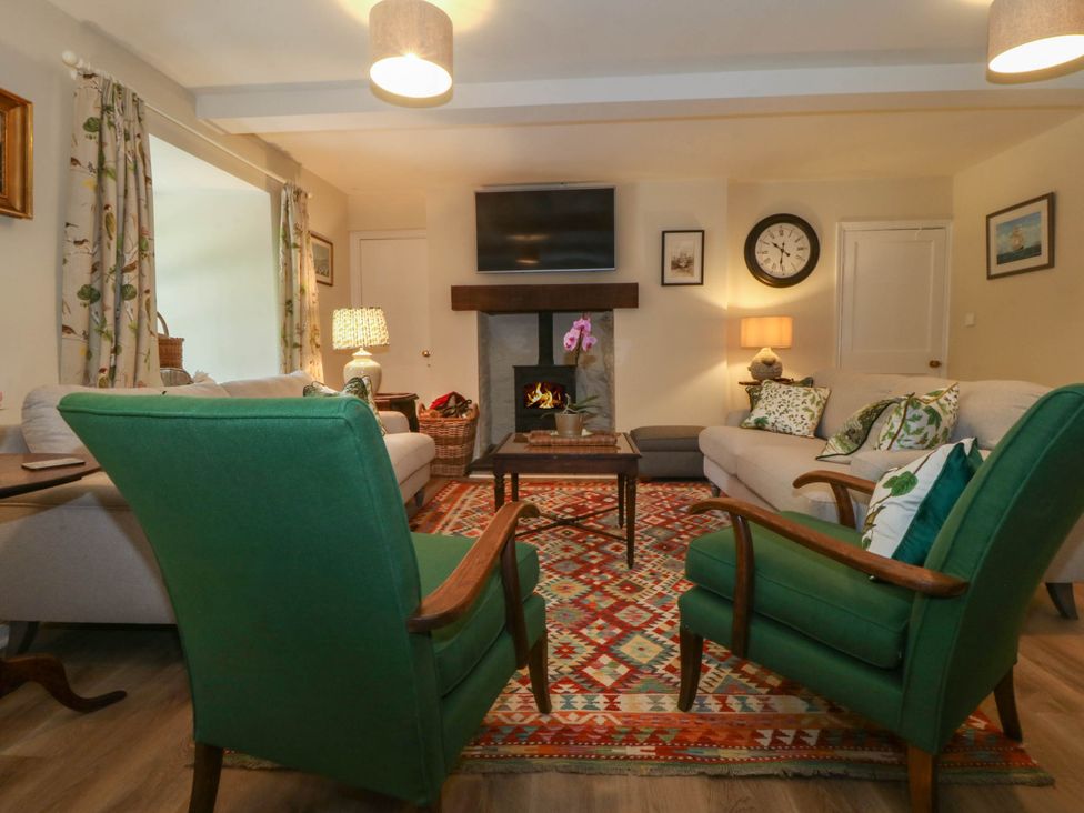 A living room with green armchairs a patterned rug a fireplace and a wall mounted TV at Bodior Garden Cottage in Rhoscolyn