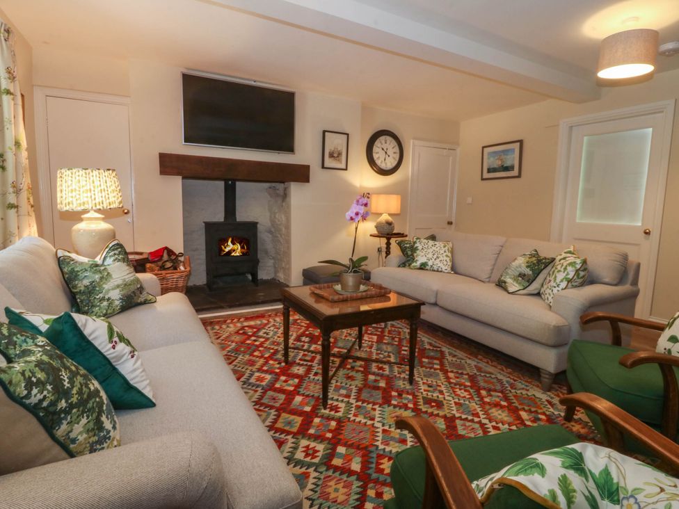 A living room with two sofas green armchairs and a patterned rug at Bodior Garden Cottage in Rhoscolyn