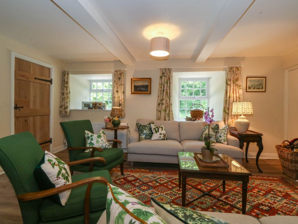 A living room with green armchairs a beige sofa and a patterned rug at Bodior Garden Cottage in Rhoscolyn