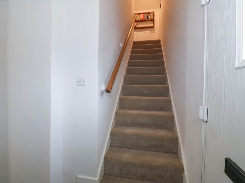 A carpeted staircase with a wooden handrail and a small bookshelf at the top at Bodior Garden Cottage in Rhoscolyn