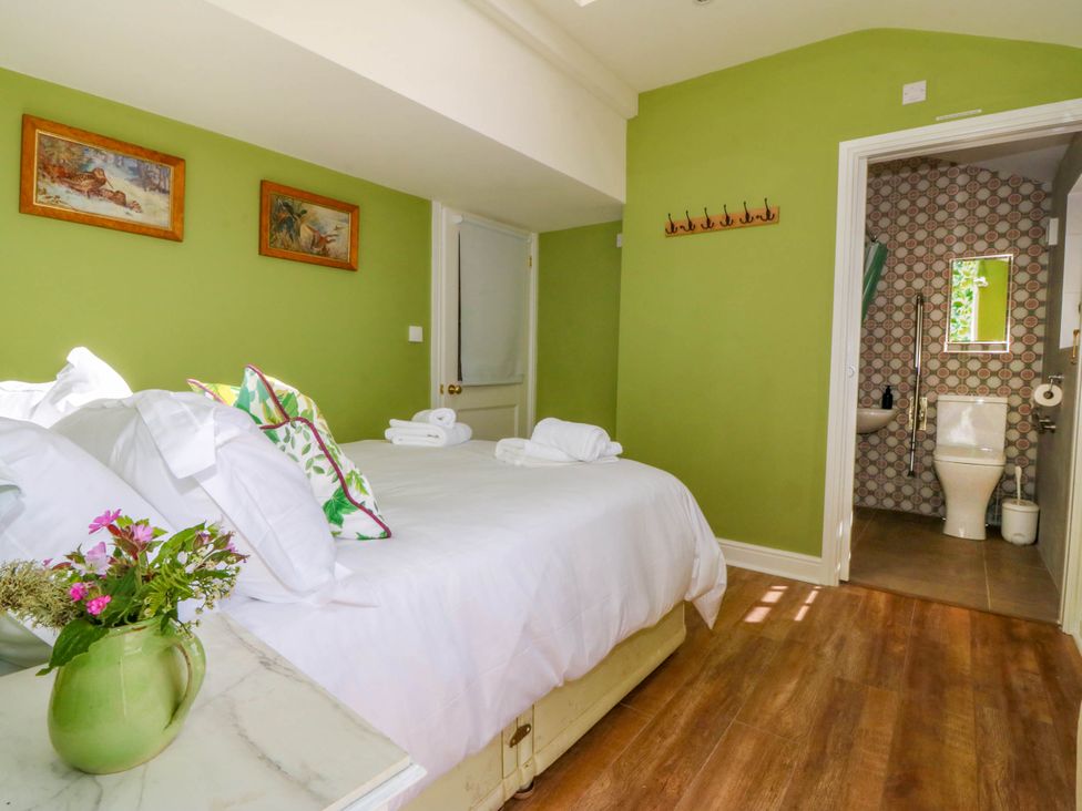A bedroom with a bed towels flowers and an attached bathroom at Bodior Garden Cottage in Rhoscolyn