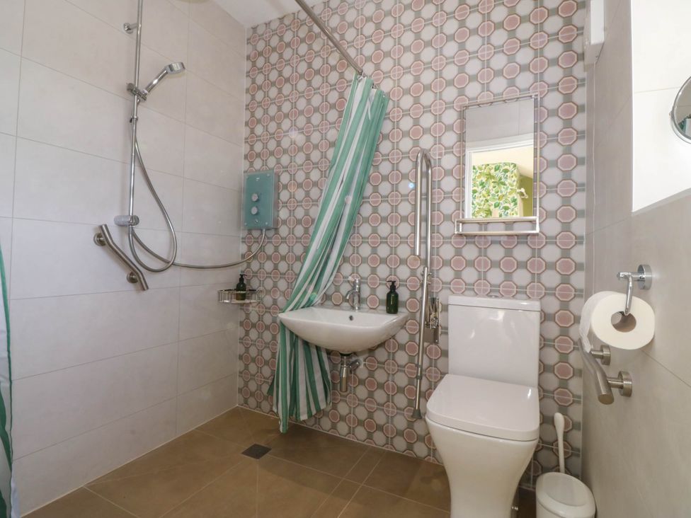 A bathroom with a shower area sink toilet mirror and striped shower curtain at Bodior Garden Cottage in Rhoscolyn