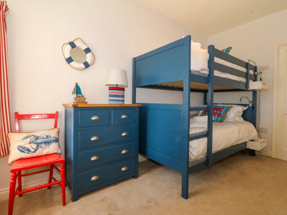 A bedroom with blue bunk beds a blue chest of drawers a red chair and nautical decor at Bodior Garden Cottage Rhoscolyn