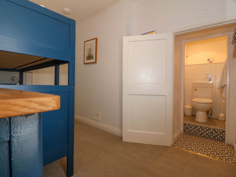 A room with a blue bunk bed and a door leading to a bathroom with a toilet at Bodior Garden Cottage in Rhoscolyn
