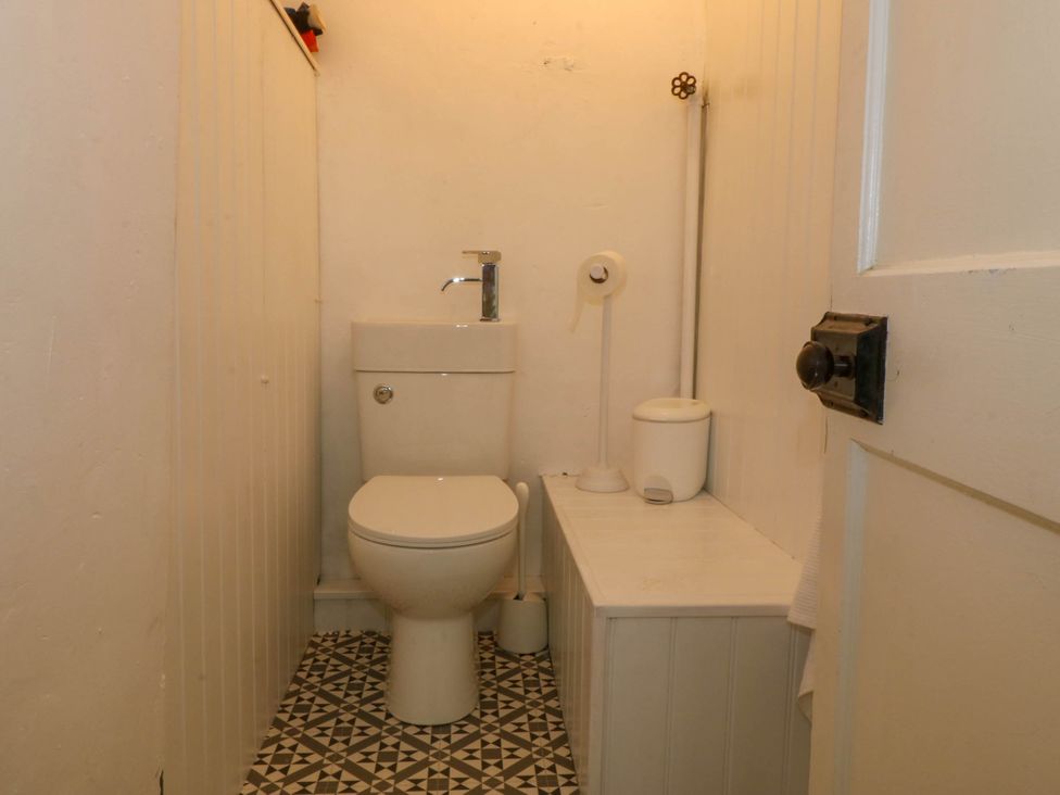 A small bathroom with a toilet a sink tap a toilet brush a toilet paper holder and a trash bin at Bodior Garden Cottage in Rhoscolyn