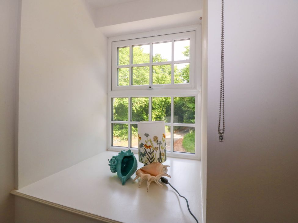 A window with a white windowsill holding two seashells and a cylindrical lamp with floral designs at Bodior Garden Cottage in Rhoscolyn