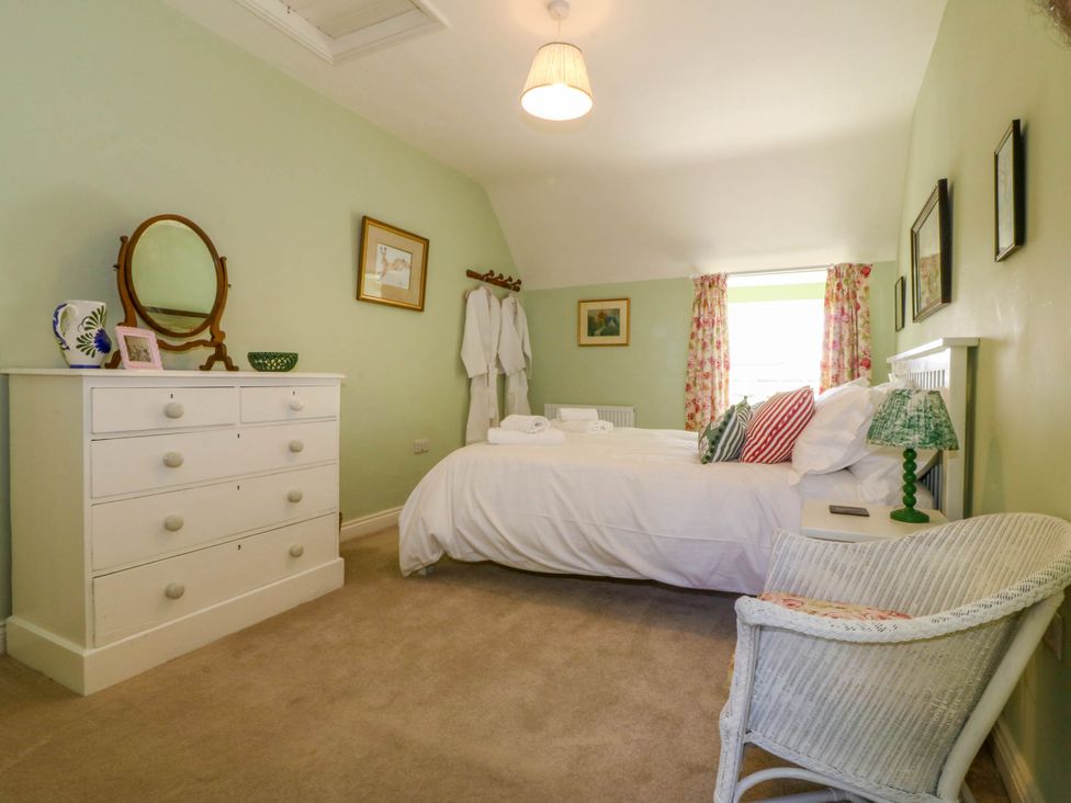 A bedroom with a bed pillows and bedside table next to a window with floral curtains at Bodior Garden Cottage in Rhoscolyn