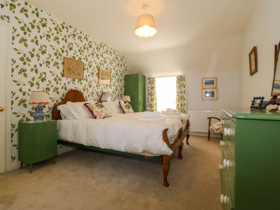 A bedroom with a double bed green bedside tables and dresser with floral wallpaper at Bodior Garden Cottage in Rhoscolyn