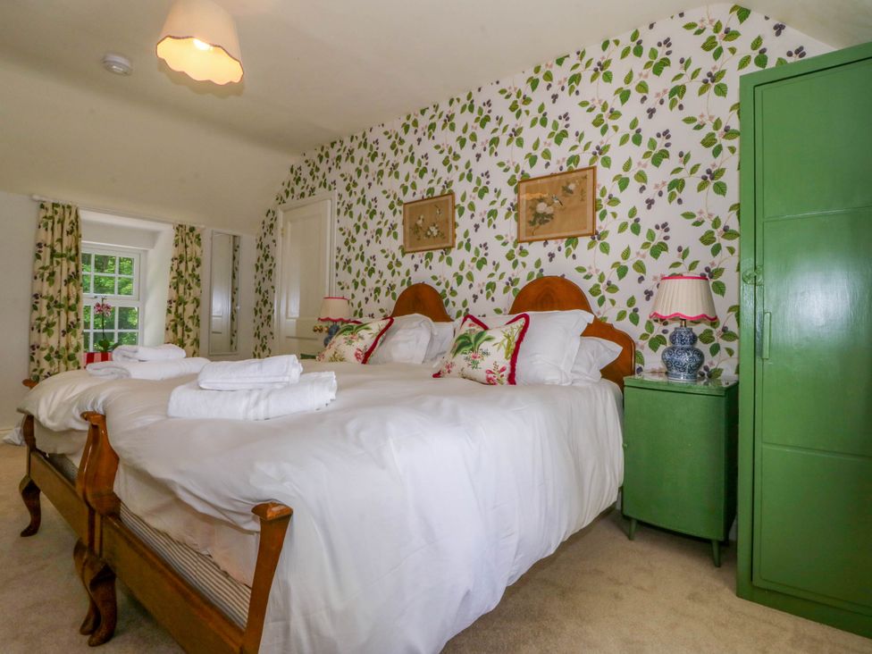 A bedroom with two single beds pushed together floral wallpaper green bedside table and wardrobe at Bodior Garden Cottage in Rhoscolyn