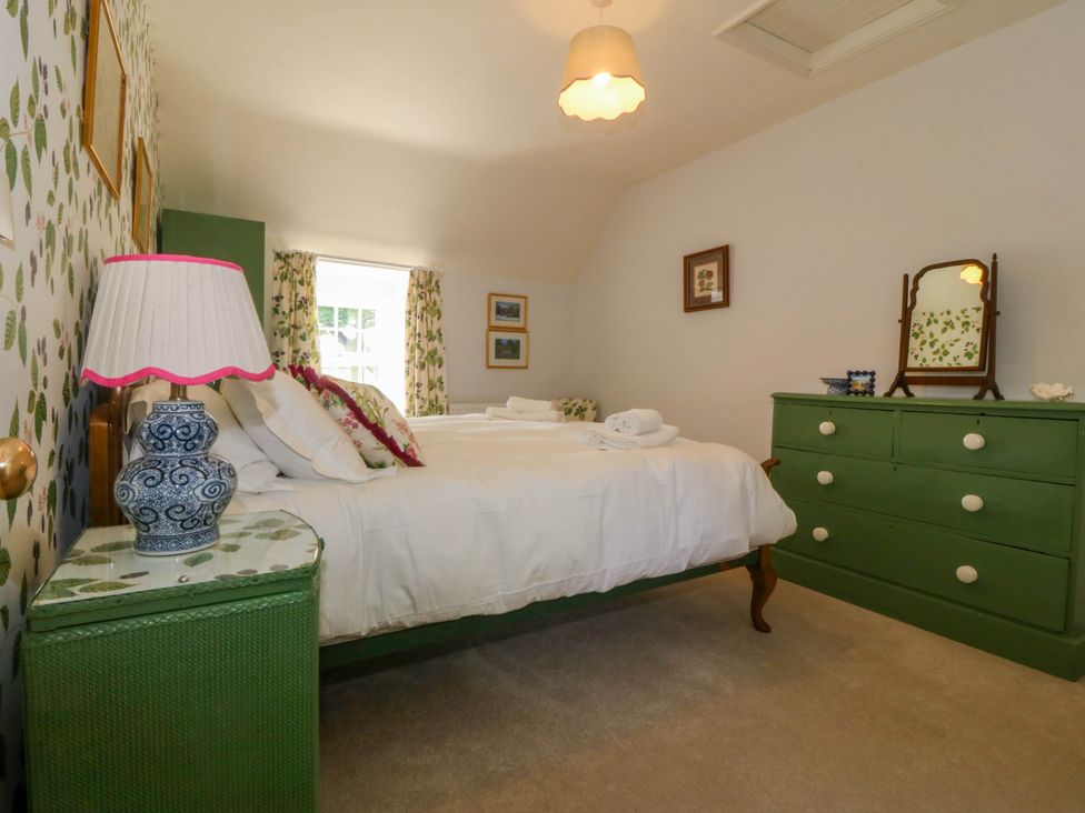 A bedroom with a bed white bedding green furniture and leaf patterned wallpaper at Bodior Garden Cottage in Rhoscolyn