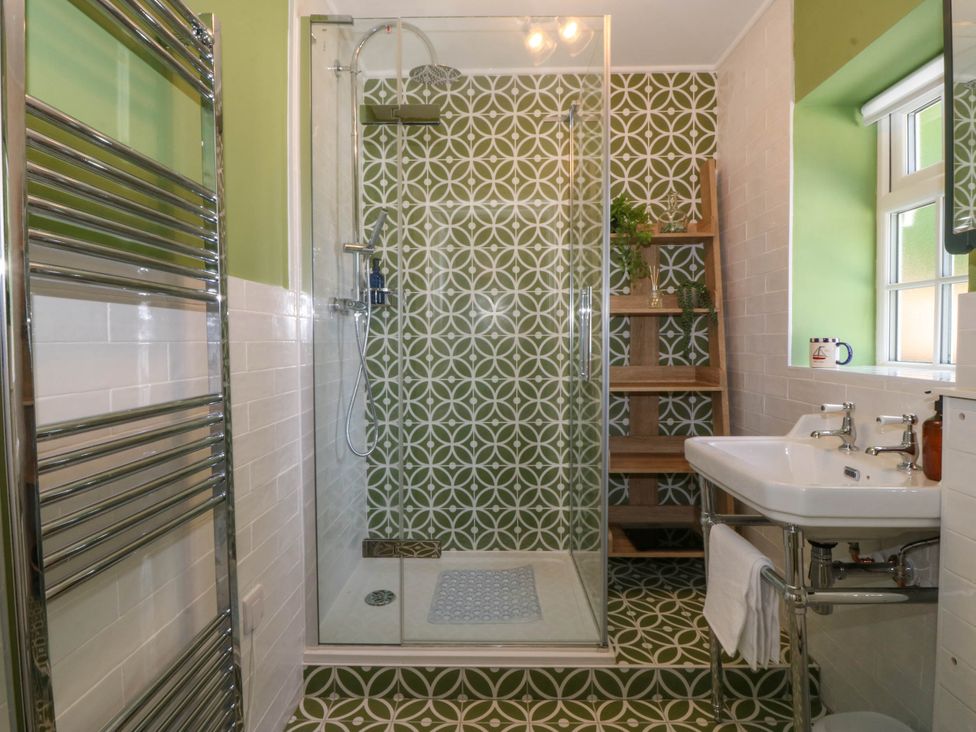 A bathroom with a glass shower enclosure and patterned green and white tiles at Bodior Garden Cottage in Rhoscolyn