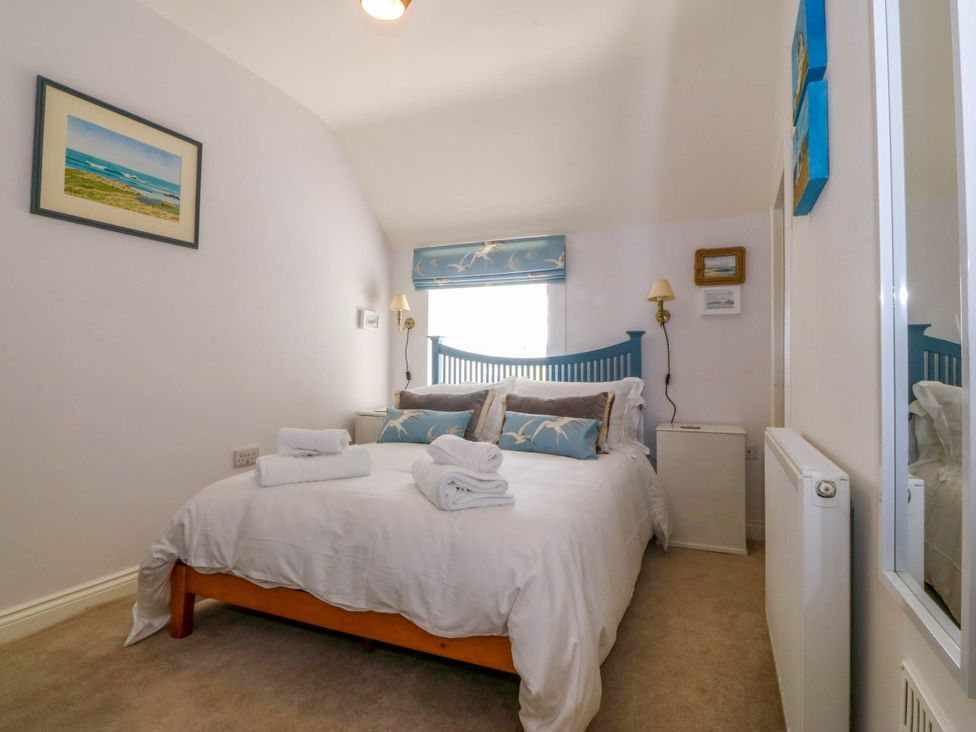 A bedroom with a double bed with white bedding and blue headboard at Bodior Garden Cottage in Rhoscolyn