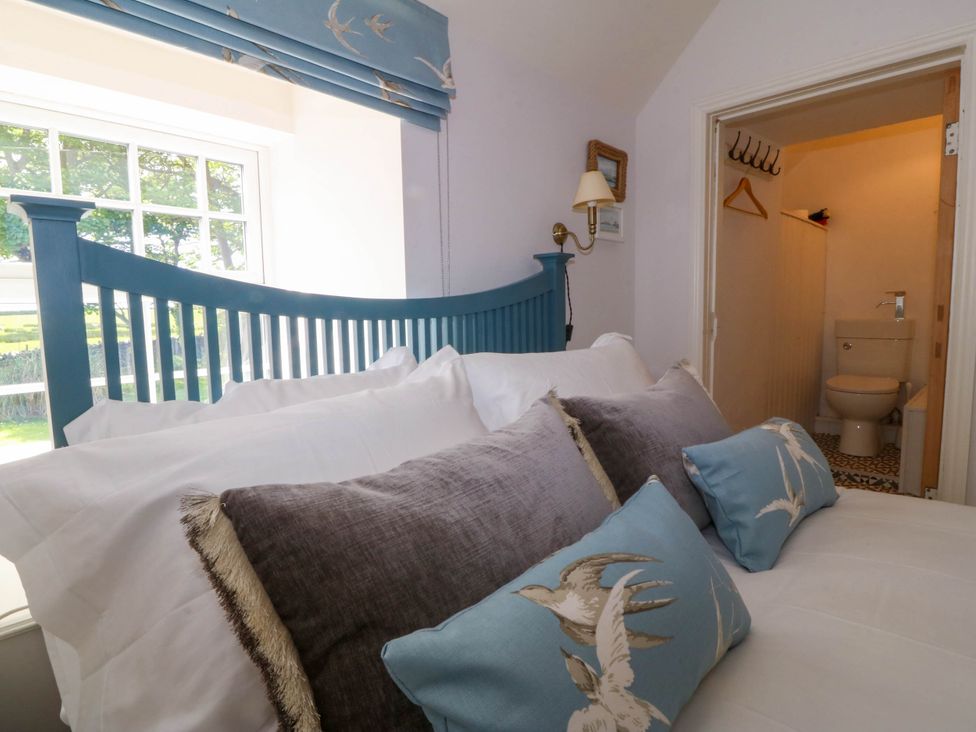 A bedroom with a blue bed frame white and blue pillows and a doorway leading to a bathroom at Bodior Garden Cottage in Rhoscolyn