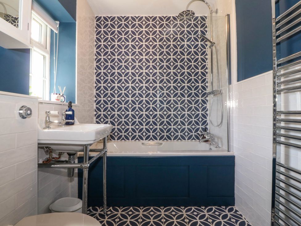 A bathroom with a bathtub shower combination a sink a toilet and patterned tiles at Bodior Garden Cottage in Rhoscolyn