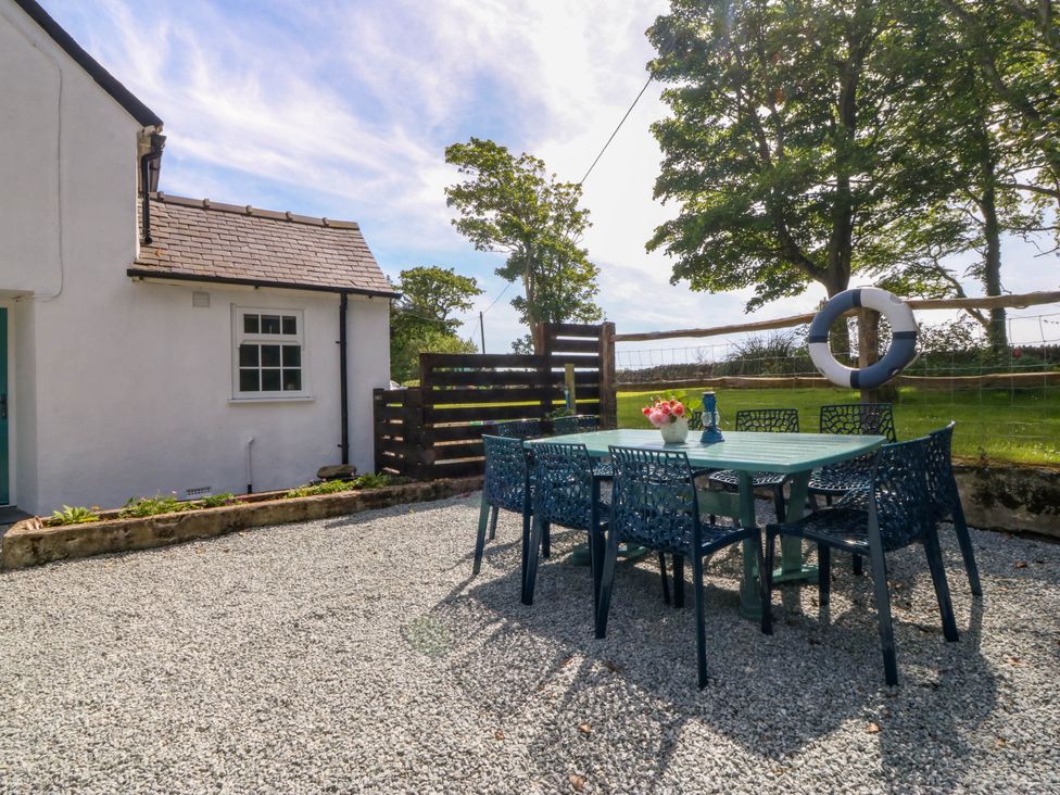 An outdoor patio with a table and six chairs next to a white house at Bodior Garden Cottage in Rhoscolyn