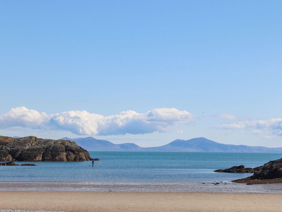 A beach with a person paddleboarding and mountains in the background at Bodior Garden Cottage Rhoscolyn