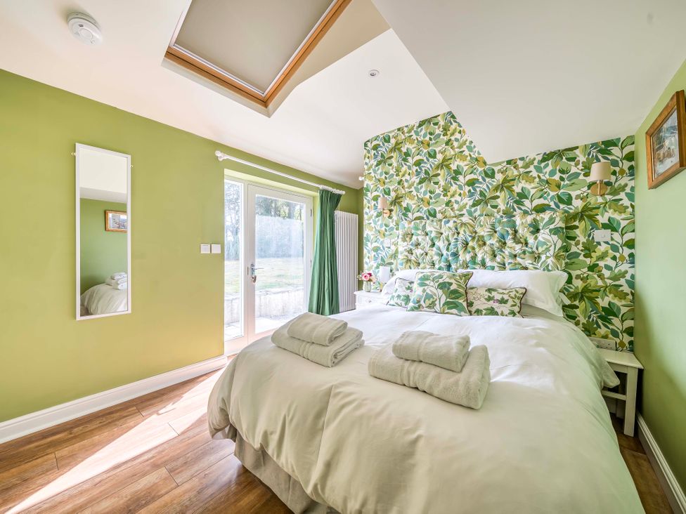 A bedroom with a bed and mirror at Bodior Garden Cottage Rhoscolyn