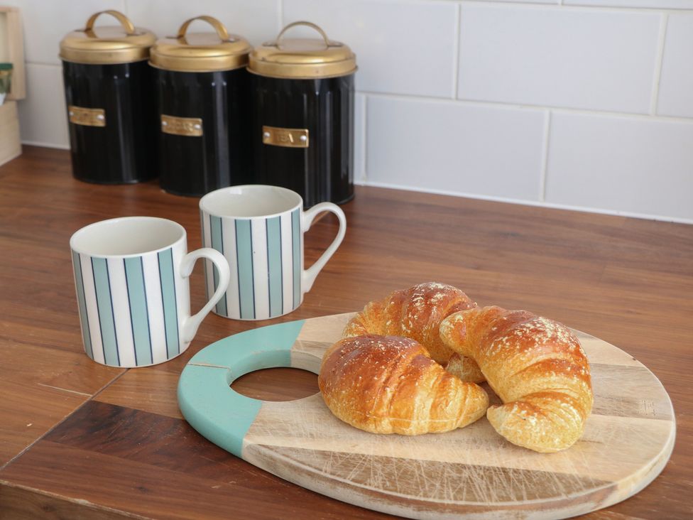 A kitchen with croissants on a cutting board and mugs on the counter at Cosy Cottage in Buxton