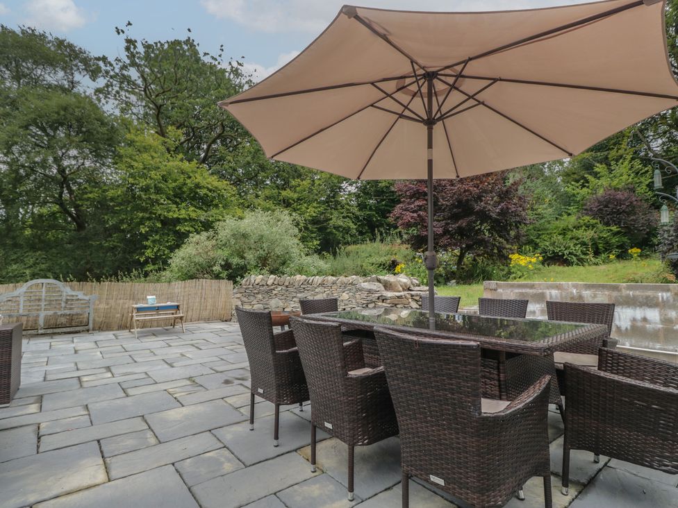 An outdoor patio with a dining table and chairs under a parasol at Whimhowe in Windermere
