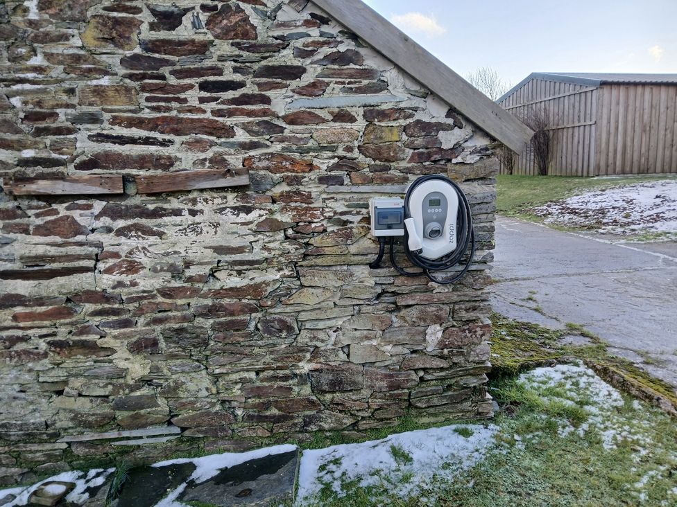 An electric vehicle charger mounted on a stone wall in an outdoor area at The Dairy Barn in Camelford