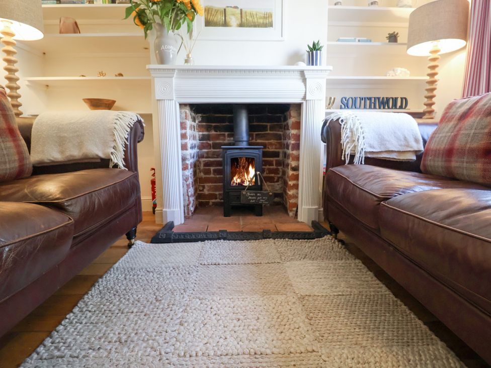 A living room with a fireplace and two sofas at Victoria Cottage (4 East Green) Southwold
