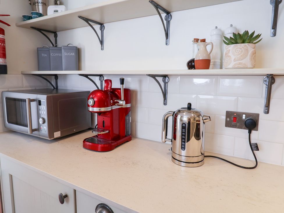 A kitchen with a microwave, espresso machine, kettle, and shelf at Victoria Cottage (4 East Green) Southwold