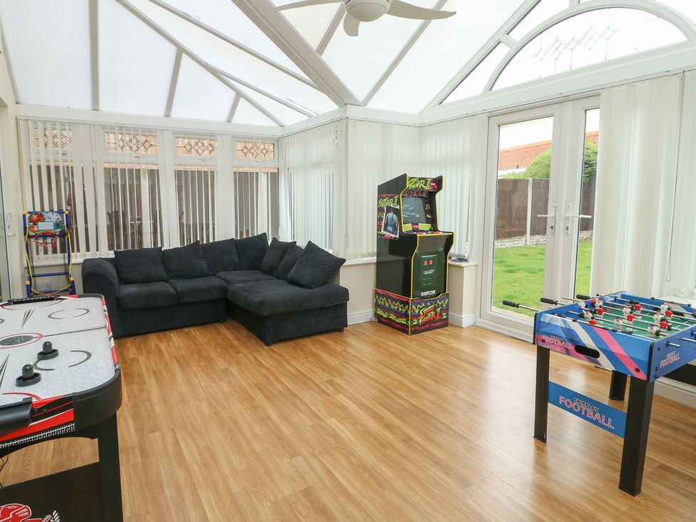 A conservatory with sofas and gaming tables at 9 Beckett Close in Colwyn Bay