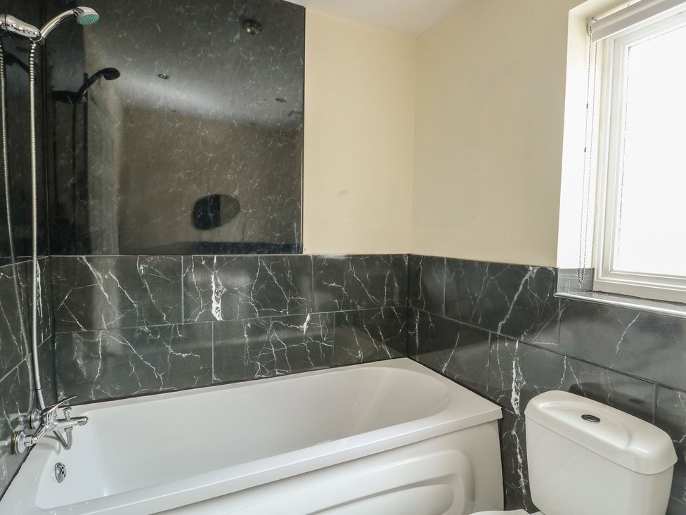 A bathroom with a bathtub, toilet, and shower at 9 Beckett Close in Colwyn Bay