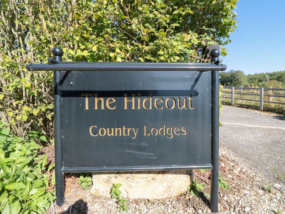 A sign for The Hideout Country Lodges with bushes and gravel at The Hideout in Thornton-Le-Dale