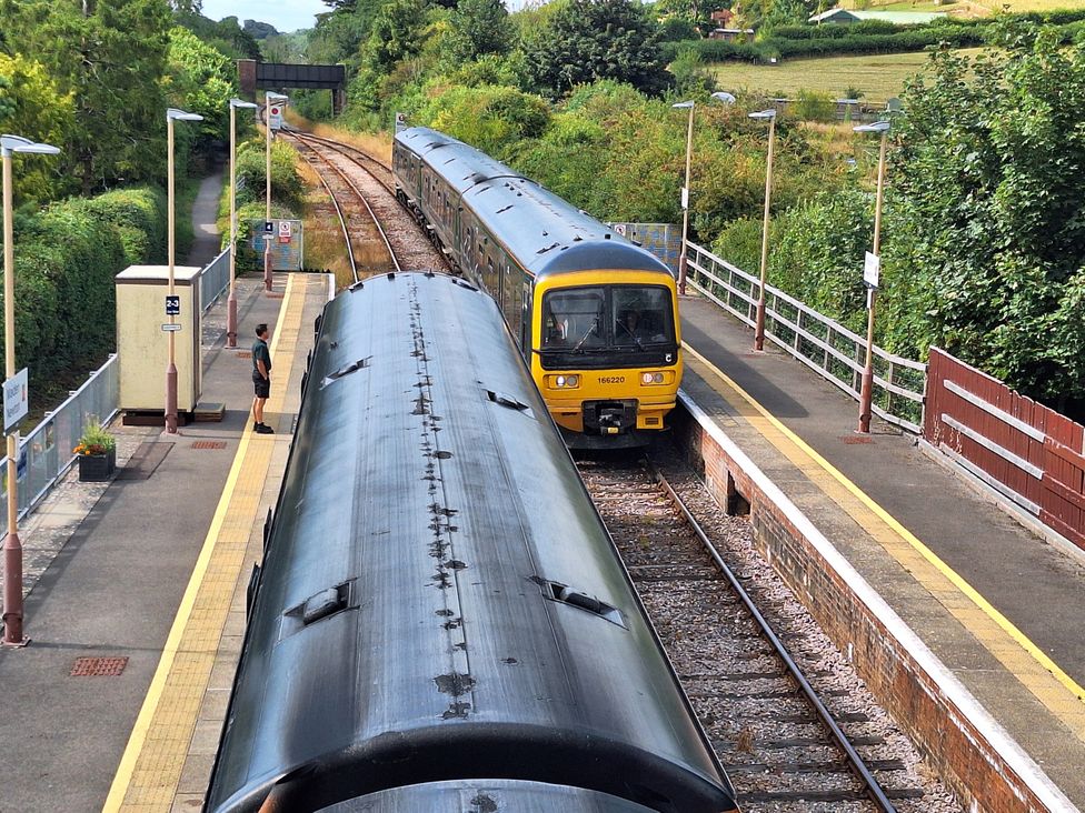 A train arriving at a platform with a person waiting at The Halt in Maiden Newton